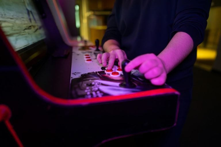 Eine Hand spielt an einem klassischen Arcade-Spieleautomat mit Joystick und Tasten.